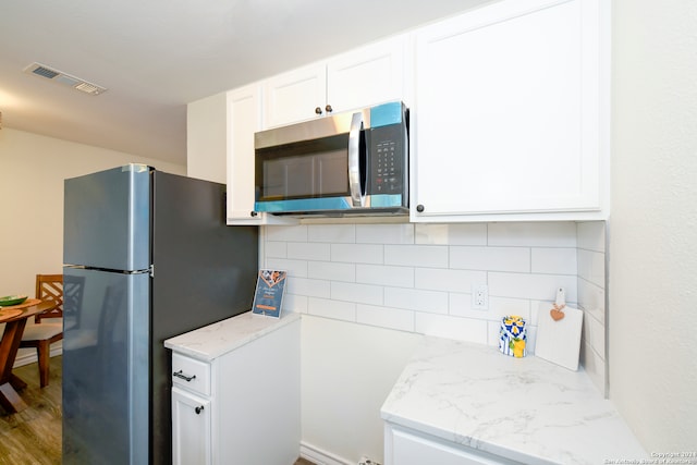 kitchen featuring appliances with stainless steel finishes, light stone counters, tasteful backsplash, white cabinets, and hardwood / wood-style floors