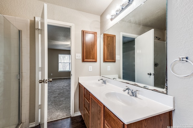 bathroom with double sink, hardwood / wood-style floors, a shower with shower door, oversized vanity, and a textured ceiling