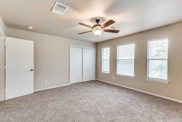 unfurnished bedroom with a closet, a textured ceiling, light colored carpet, and ceiling fan