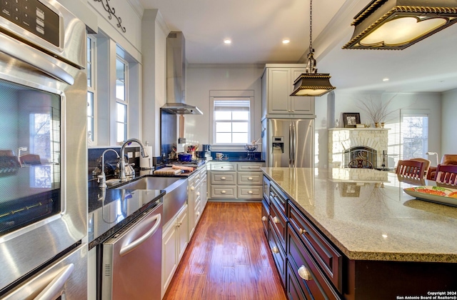 kitchen with wall chimney exhaust hood, appliances with stainless steel finishes, white cabinetry, and a fireplace