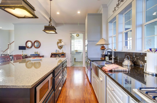 kitchen featuring pendant lighting, dark stone counters, appliances with stainless steel finishes, white cabinetry, and light wood-type flooring