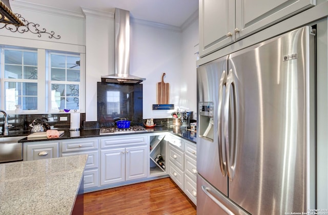 kitchen featuring light hardwood / wood-style floors, white cabinetry, dark stone countertops, stainless steel appliances, and wall chimney exhaust hood