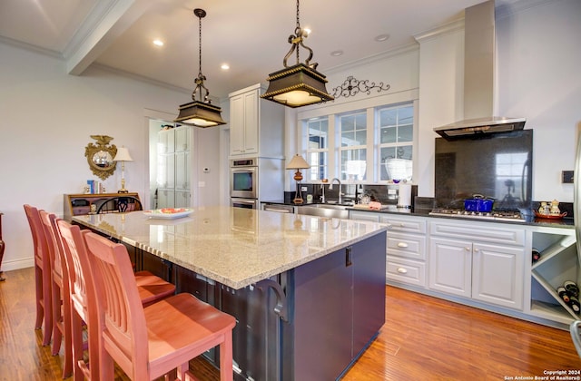 kitchen featuring light stone counters, a kitchen bar, sink, wall chimney exhaust hood, and white cabinets