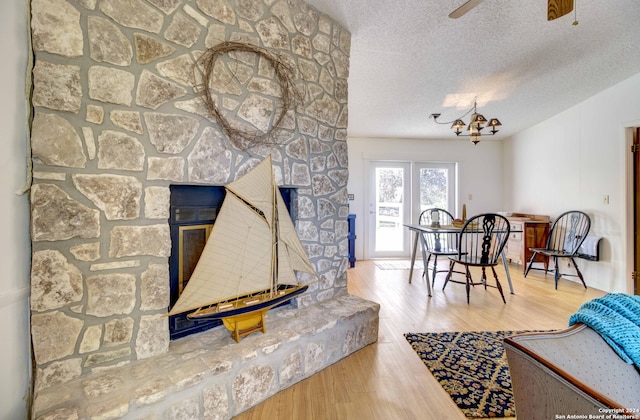 living room with a textured ceiling, a stone fireplace, light hardwood / wood-style floors, and ceiling fan with notable chandelier