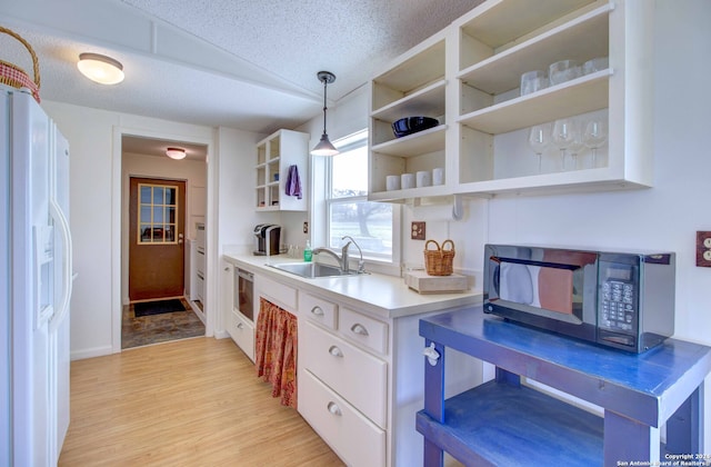 kitchen with hanging light fixtures, white fridge with ice dispenser, sink, light hardwood / wood-style flooring, and a textured ceiling