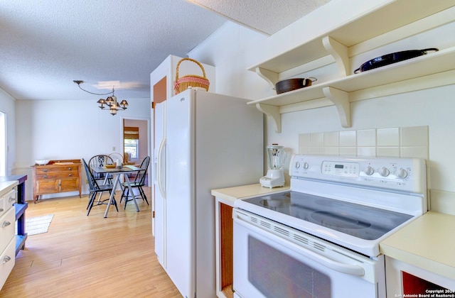 kitchen featuring a chandelier, a textured ceiling, light hardwood / wood-style flooring, white appliances, and hanging light fixtures