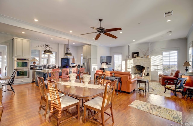 dining area with plenty of natural light, light hardwood / wood-style flooring, ceiling fan, and a stone fireplace