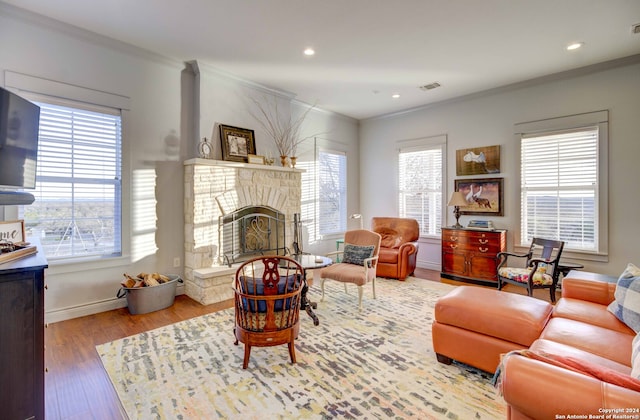 living room featuring plenty of natural light, a stone fireplace, wood-type flooring, and crown molding