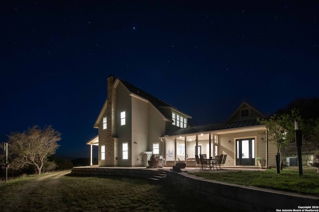 back house at twilight featuring central AC, a lawn, and a patio