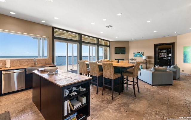 interior space featuring stainless steel dishwasher, a water view, a kitchen island, light tile floors, and sink