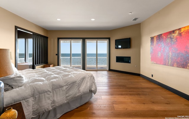 bedroom featuring a water view, access to exterior, and light hardwood / wood-style flooring