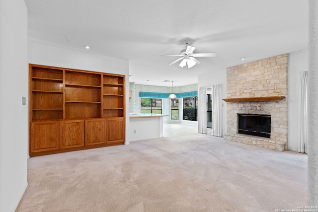 unfurnished living room with light carpet, ceiling fan, and a stone fireplace