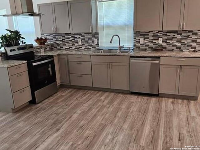 kitchen with appliances with stainless steel finishes, wall chimney exhaust hood, light stone countertops, and sink