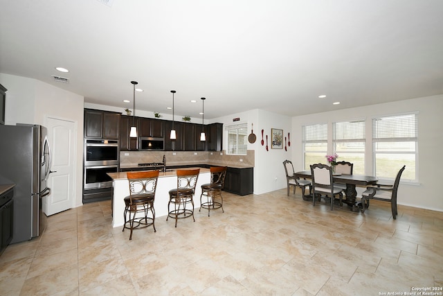 interior space featuring a breakfast bar area, light tile floors, stainless steel appliances, backsplash, and hanging light fixtures