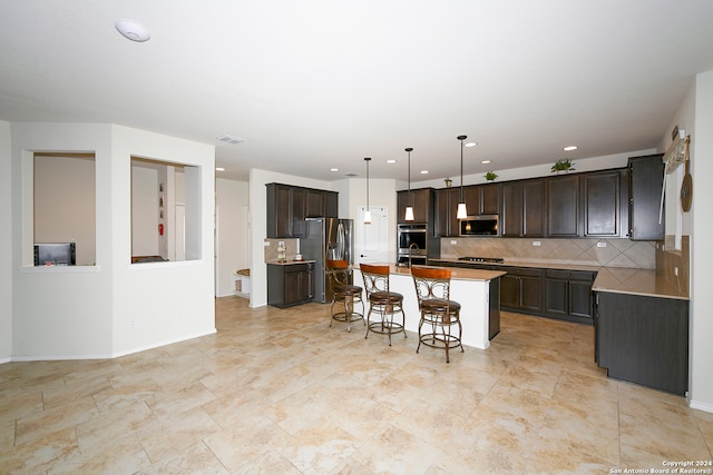 kitchen with an island with sink, stainless steel appliances, a breakfast bar, dark brown cabinets, and hanging light fixtures