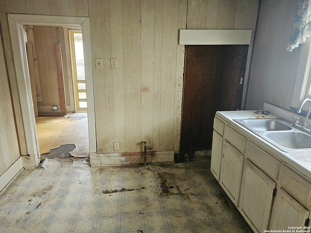 kitchen with wood walls, cream cabinets, dark tile floors, and sink