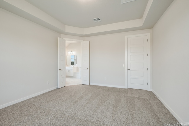 unfurnished bedroom featuring light colored carpet, ensuite bathroom, and a raised ceiling