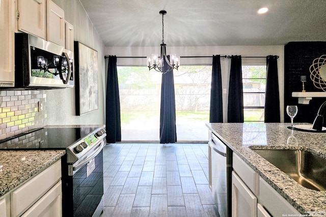 kitchen with an inviting chandelier, light stone counters, tasteful backsplash, stainless steel appliances, and sink