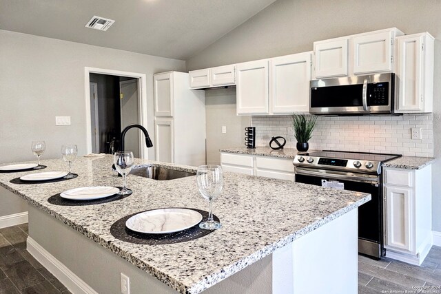 kitchen featuring white cabinets, stainless steel appliances, light stone countertops, sink, and vaulted ceiling