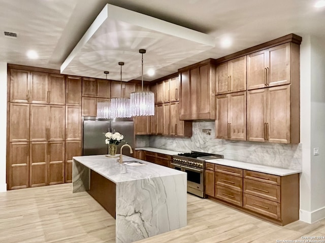 kitchen featuring light wood-type flooring, light stone countertops, hanging light fixtures, appliances with stainless steel finishes, and sink