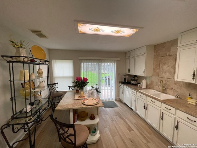 kitchen featuring light wood-type flooring, decorative backsplash, sink, and white cabinets