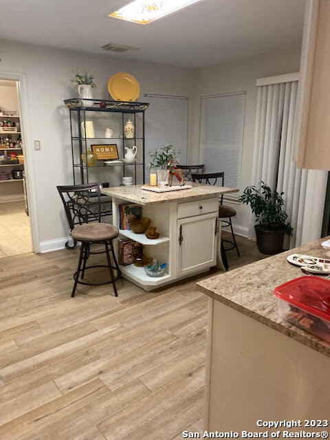 kitchen with light wood-type flooring, light stone counters, a center island, a breakfast bar, and white cabinets