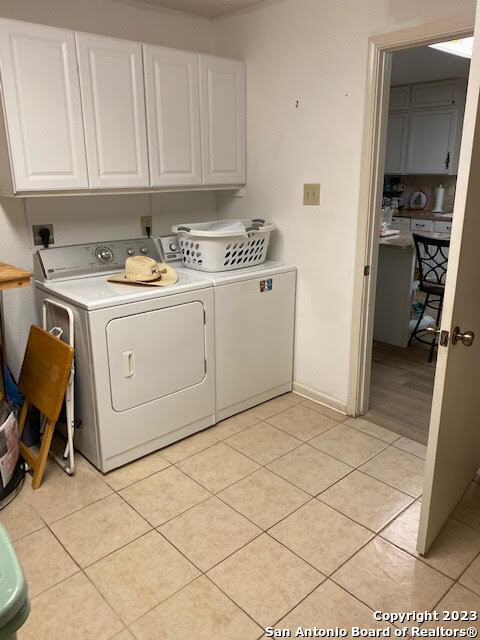 clothes washing area with light tile patterned flooring, washing machine and dryer, and cabinets