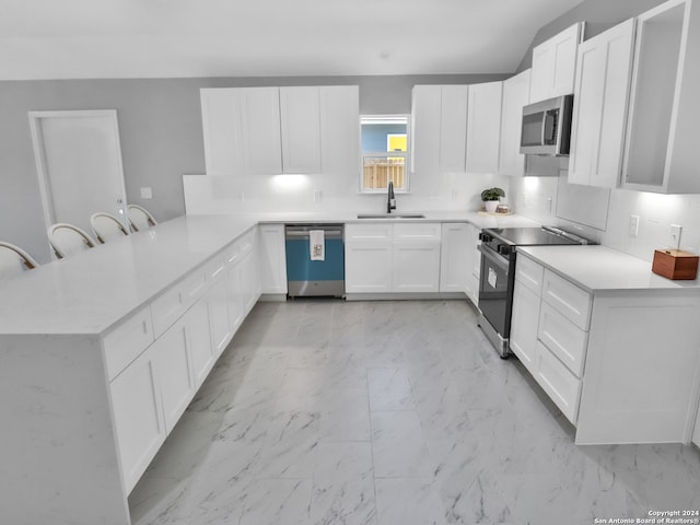 kitchen with sink, kitchen peninsula, white cabinetry, stainless steel appliances, and a breakfast bar