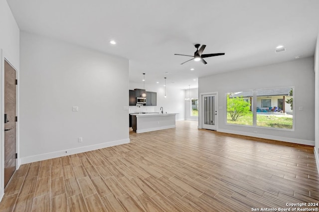 unfurnished living room with sink, ceiling fan, and light hardwood / wood-style flooring