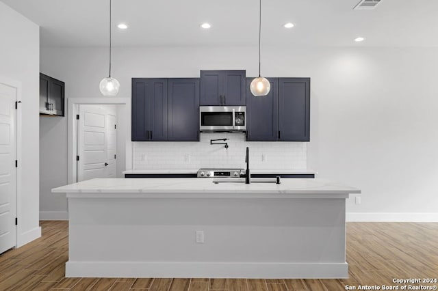 kitchen featuring light stone countertops, decorative light fixtures, light hardwood / wood-style floors, and an island with sink