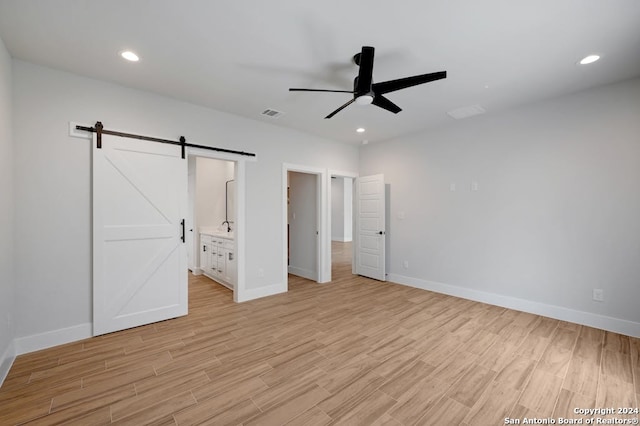 unfurnished bedroom featuring ceiling fan, light wood-type flooring, ensuite bath, and a barn door