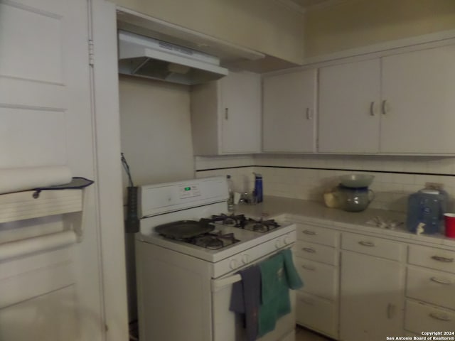 kitchen with wall chimney exhaust hood, tasteful backsplash, white gas range oven, and white cabinetry