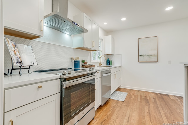 kitchen featuring white cabinetry, light hardwood / wood-style floors, stainless steel appliances, wall chimney range hood, and tasteful backsplash