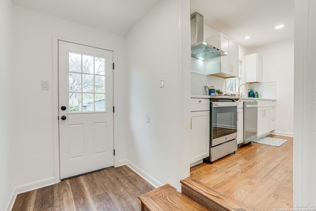 interior space with wall chimney exhaust hood, range, white cabinets, and light wood-type flooring