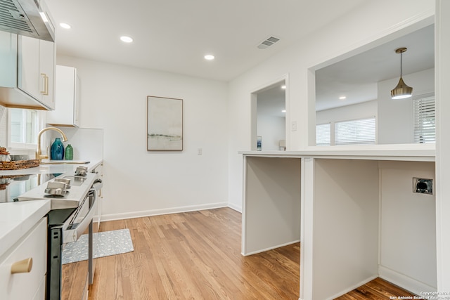 kitchen with light hardwood / wood-style floors, white cabinets, wall chimney range hood, electric range oven, and pendant lighting