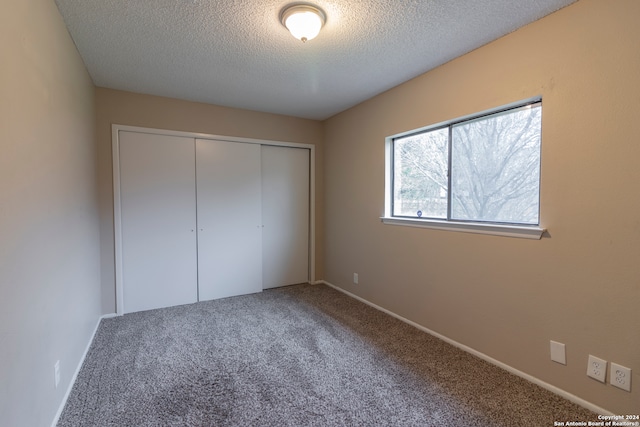 unfurnished bedroom with a textured ceiling, carpet floors, and a closet