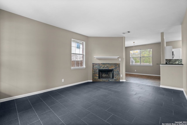 unfurnished living room featuring dark tile floors, a notable chandelier, and a fireplace