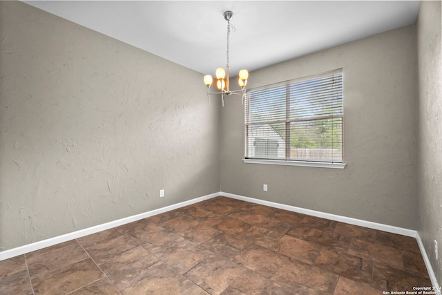 empty room with a notable chandelier and dark tile flooring