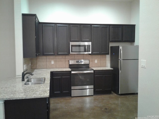 kitchen with backsplash, light stone counters, appliances with stainless steel finishes, and sink