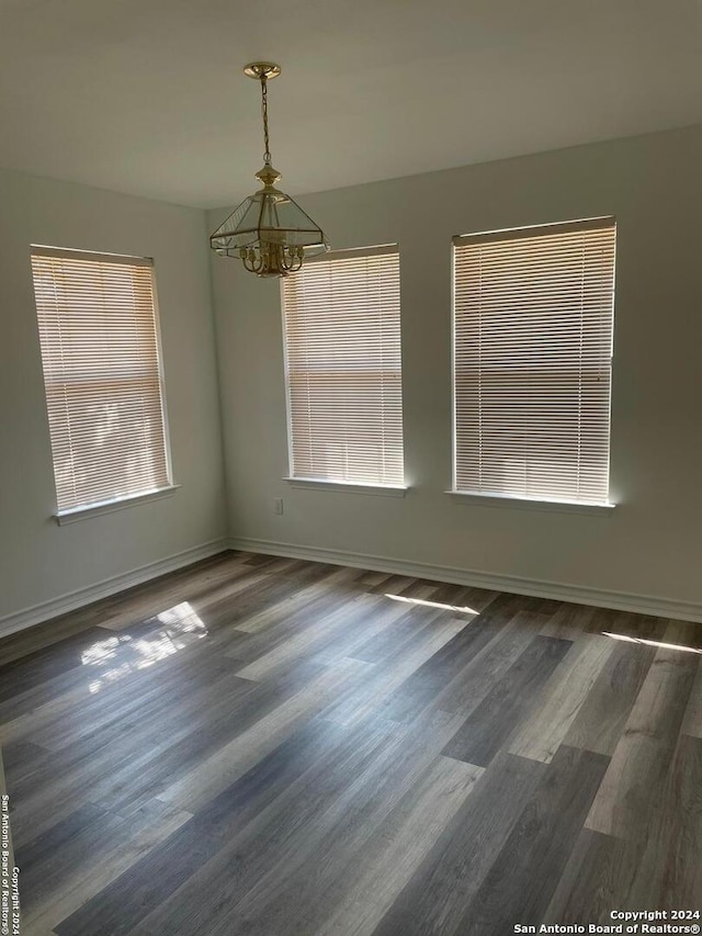 unfurnished room featuring a chandelier, a healthy amount of sunlight, and dark wood-type flooring