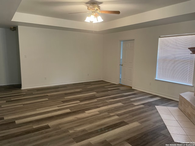 unfurnished room featuring a raised ceiling, ceiling fan, and dark hardwood / wood-style floors