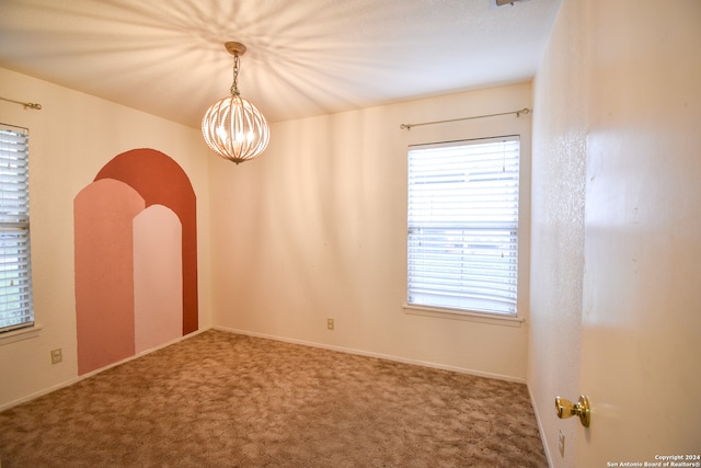 unfurnished room with a chandelier, dark carpet, and a wealth of natural light