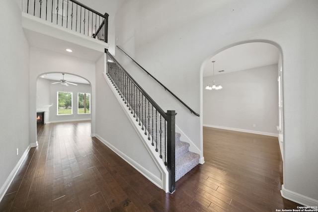 staircase featuring ceiling fan with notable chandelier, a towering ceiling, and dark hardwood / wood-style flooring