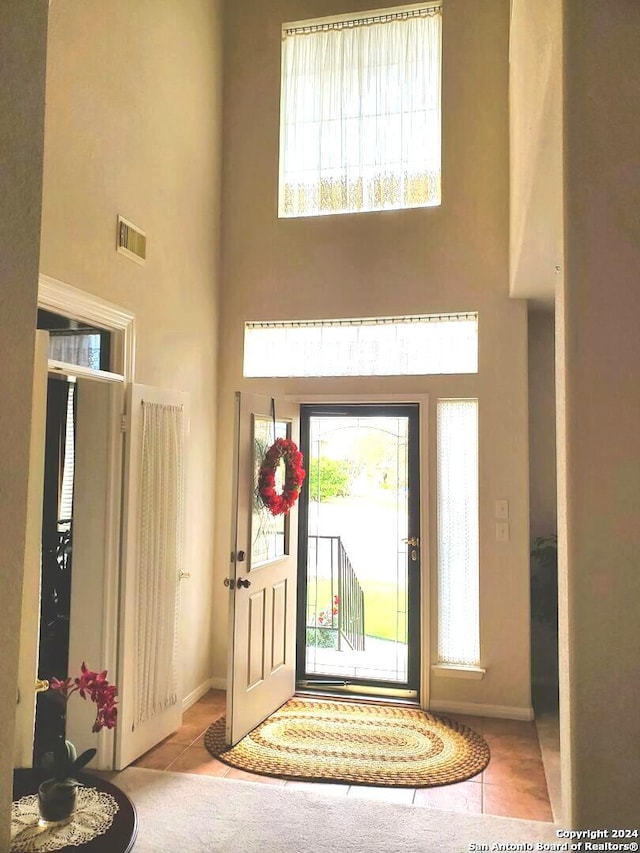 foyer with a high ceiling, light tile patterned flooring, visible vents, and baseboards