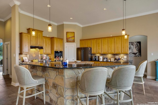 kitchen with decorative light fixtures, tasteful backsplash, a breakfast bar area, dark tile floors, and black fridge