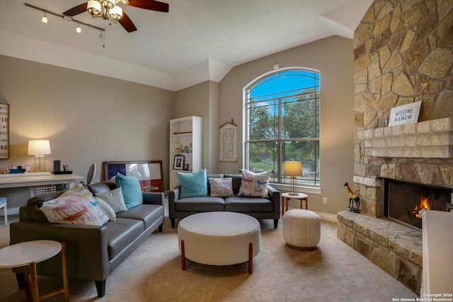 living room with light colored carpet, ceiling fan, rail lighting, a stone fireplace, and lofted ceiling