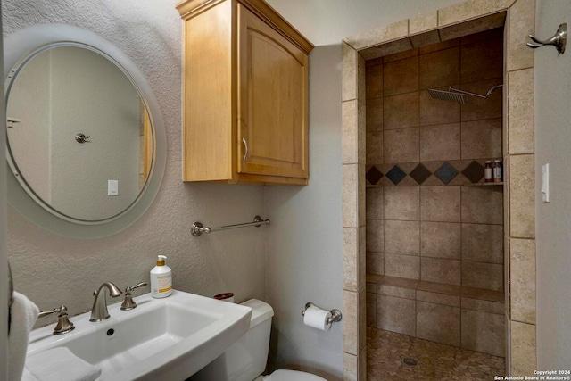 bathroom with toilet, sink, and tiled shower