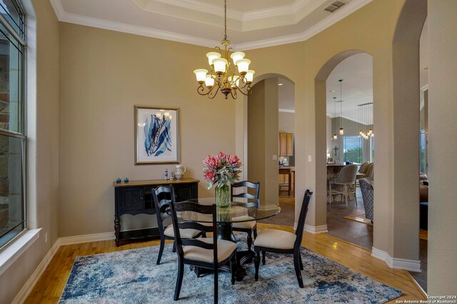 dining area with a raised ceiling, crown molding, a notable chandelier, and light hardwood / wood-style flooring