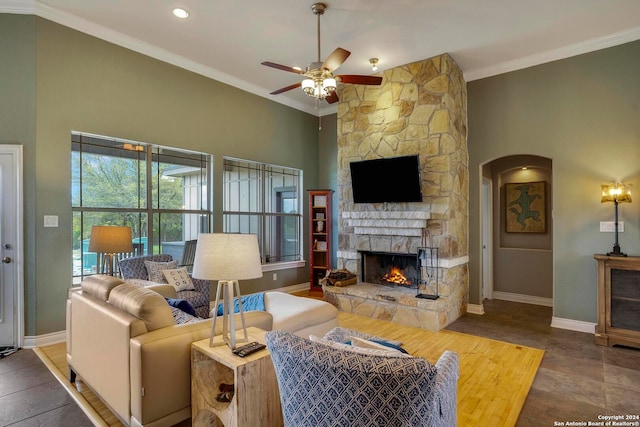 living room featuring dark tile flooring, a stone fireplace, crown molding, and ceiling fan