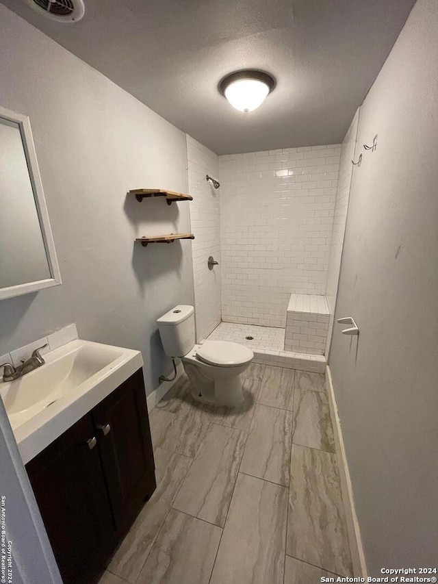 bathroom featuring vanity, tile floors, toilet, and tiled shower